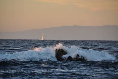 Waves flowing in sea against sky during sunset