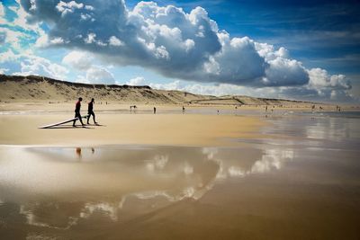 People walking on shore at beach against sky