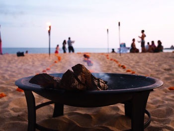 Close-up of fire pit on beach against sky during sunset