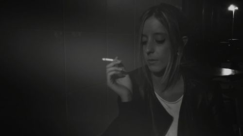 Young woman smoking cigarette by tiled wall