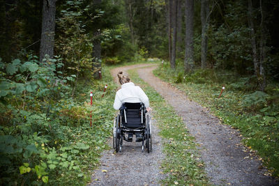 Rear view of disabled woman in wheelchair on dirt road at forest