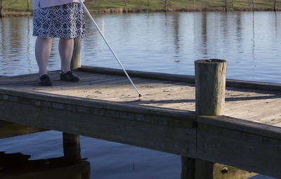 Low section of blind woman standing on pier over lake
