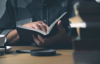 Midsection of man reading book while sitting on table