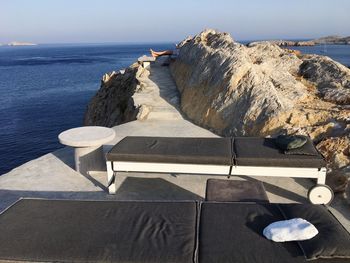 Lounge chairs on rocks by sea against sky