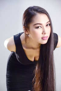 Portrait of beautiful young woman in dress bending against gray background