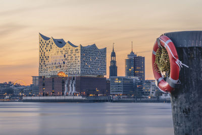 Germany, hamburg, life belt hanging on coastal post at dusk with elbphilharmonie in background