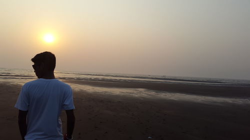 Rear view of woman standing on beach against clear sky