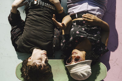 Smiling teenage boy and girl lying on skateboard over footpath during sunny day