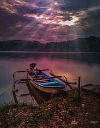 Boat moored on lake against sky during sunset