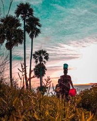 Man sitting by palm trees on beach against sky