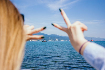 Cropped image of hand against sea against sky