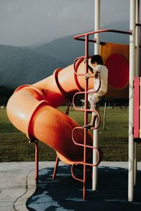 Boy climbing on pole in playground against mountains