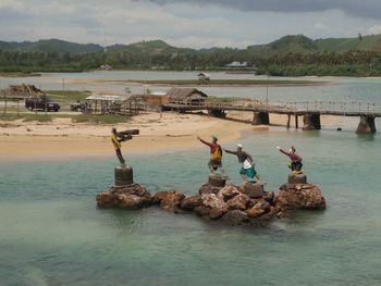 People on rocks by sea against sky