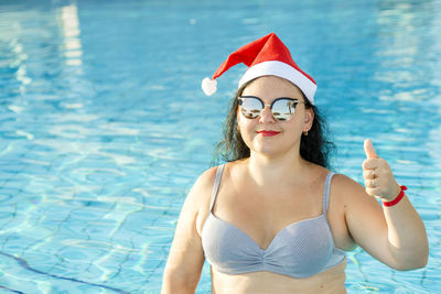 A woman in a santa hat and sunglasses in the pool celebrates christmas and shows her class 