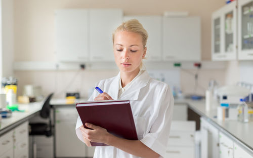 Beautiful woman writing in diary while standing at laboratory