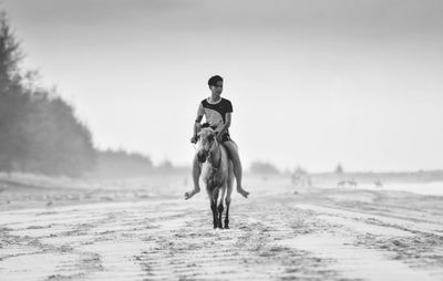 Man riding horse on sand at beach against clear sky