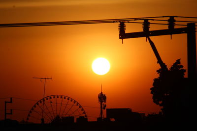 Silhouette cranes against orange sky during sunset
