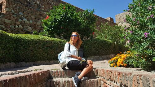 Side view of woman wearing sunglasses sitting against plants