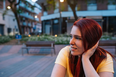 Smiling young woman looking away while sitting on footpath