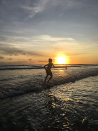 Silhouette woman standing at beach against sky during sunset