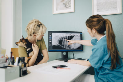 Female veterinarian showing x-ray on computer to woman with dog in doctor's office