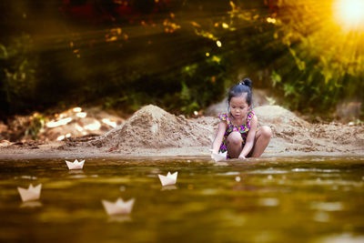 Girl sailing paper boats on lake in forest