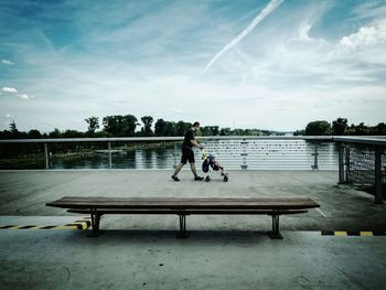 Side view of father carrying son on baby stroller by lake