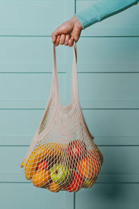 Arm of man holding reusable cotton mesh bag with fresh fruits
