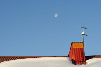 Tv antenna at house rooftop after snowfall in winter season, morning moon at blue sky