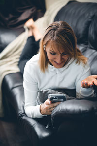 Smiling woman using mobile phone while lying on sofa at home