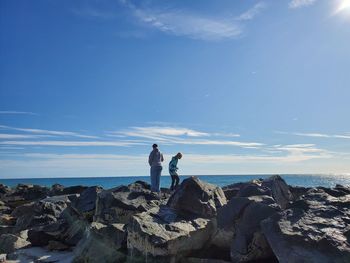 People standing on rock by sea against blue sky