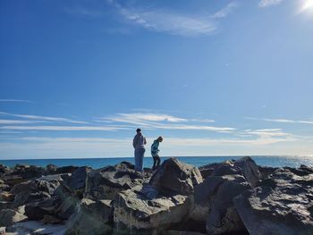 Mother and son standing on rocks by sea against sky