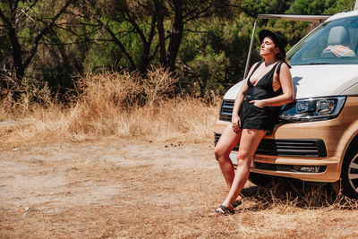 Full length of woman standing by car against trees