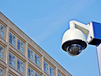 Low angle view of surveillance camera and building against blue sky