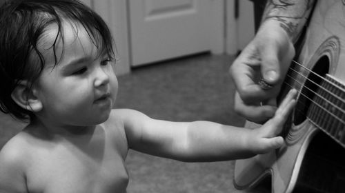 Close-up of toddler touching guitar while standing by men