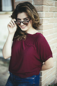 Portrait of smiling young woman in sunglasses standing against wall