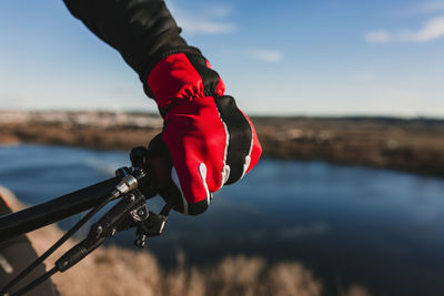 Cropped hand of person riding bicycle by river against sky