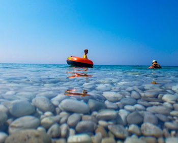 Water surface shot of siblings swimming in sea against clear blue sky during sunny day