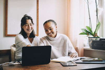 Smiling teenage girls working over laptop while studying at table in living room