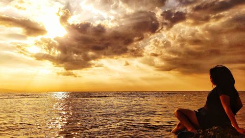 Woman looking at sea against sky during sunset