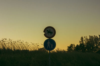 Road sign on field against sky during sunset