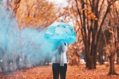 Woman with umbrella and distress flare standing at park during autumn