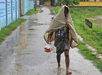 Rear view of woman walking on wet footpath in rainy season