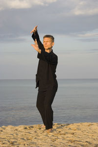 Full length of man performing tai chi while standing against sky