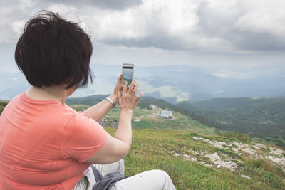 Rear view of man photographing on mobile phone against sky