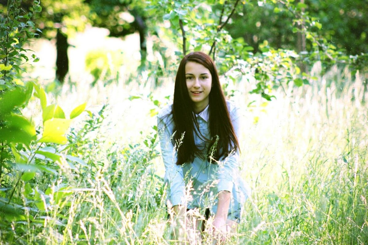 young adult, looking at camera, portrait, grass, person, plant, lifestyles, young women, flower, field, front view, growth, standing, leisure activity, casual clothing, smiling, three quarter length, tree