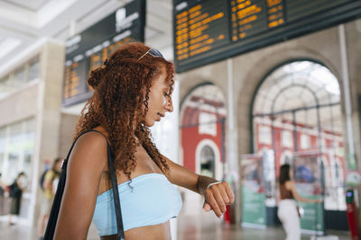 Young woman checking time on wrist watch standing at railroad station