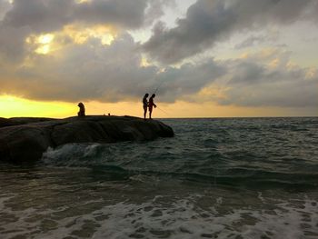 Silhouette people on beach against dramatic sky