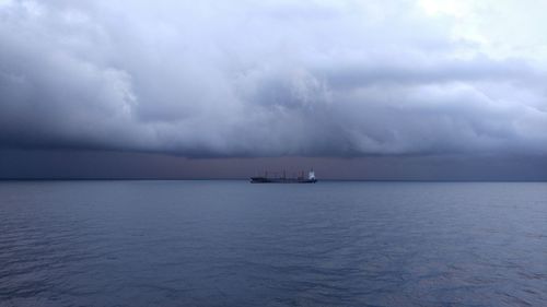 Scenic view of ship in sea against storm clouds