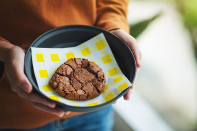 Closeup image of a woman holding a chocolate cookie in a plate